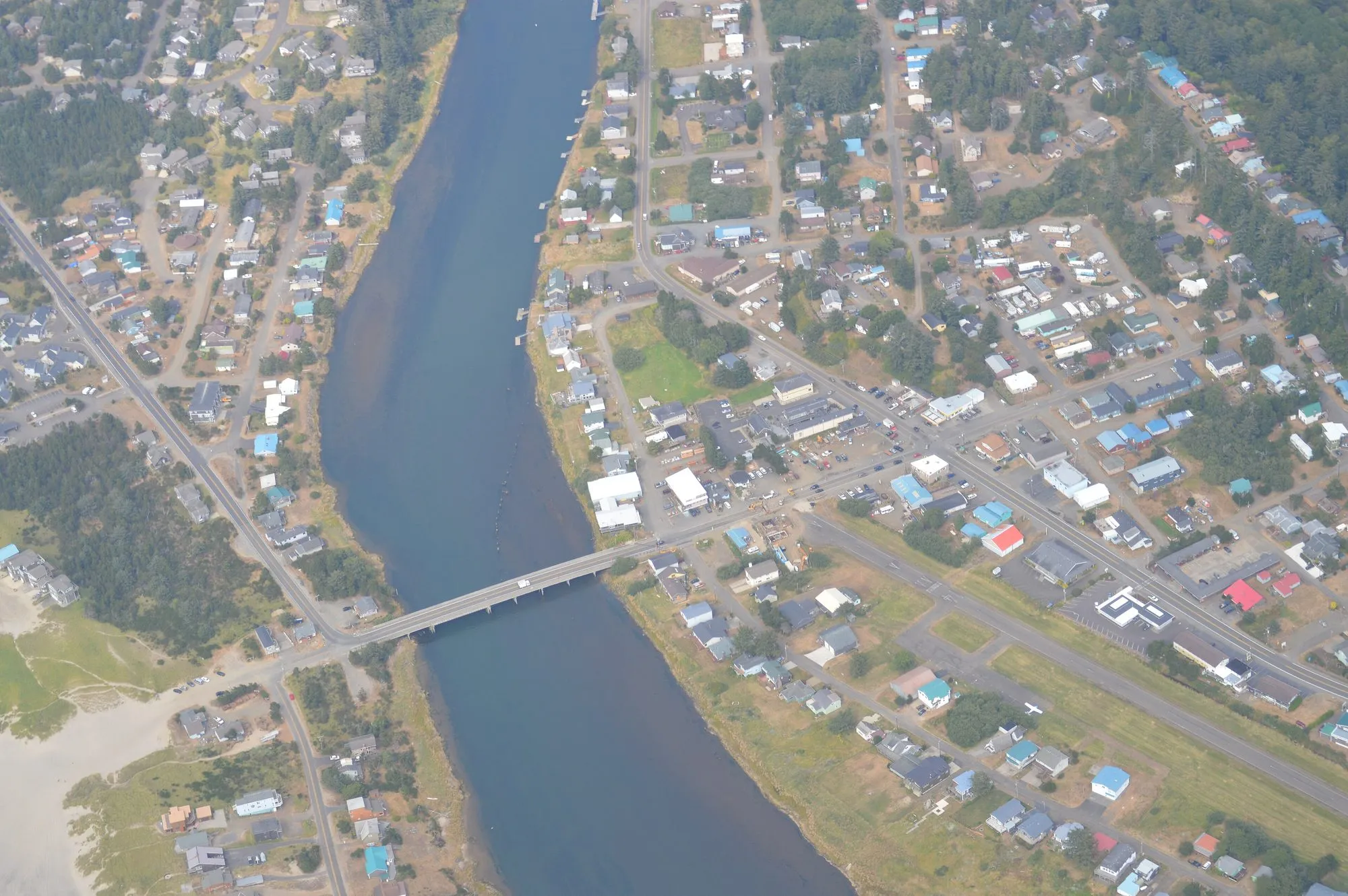 Pacific City from the air, a few streets of houses on both banks of the Nestucca River, joined by a single bridge.
