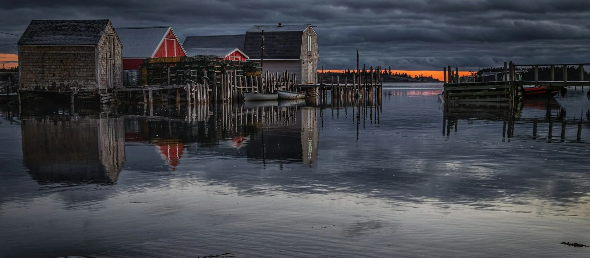 Wooden fishing buildings and wharves reflect in the water at Blue Rocks, Nova Scotia, at dusk.