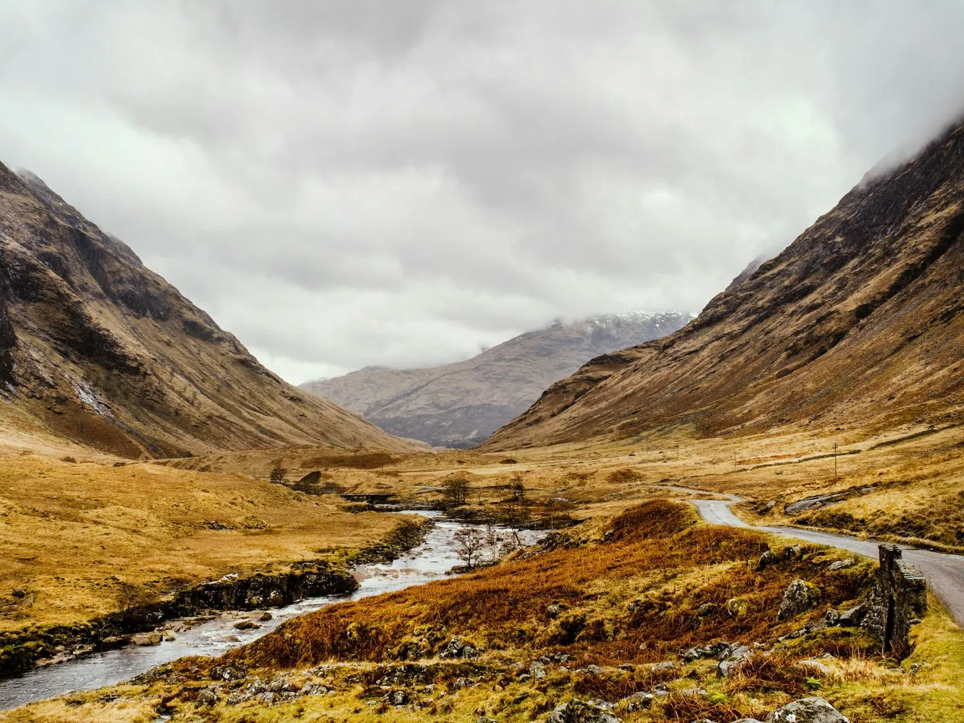Glen Etive in autumn colours, with a single-track road winding down the glen beside the river under low cloud.