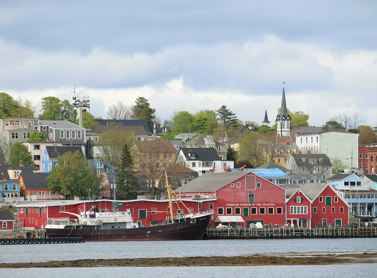 The red wharf buildings of the Fisheries Museum of the Atlantic on the Lunenburg waterfront, with a fishing vessel alongside and the town rising behind.