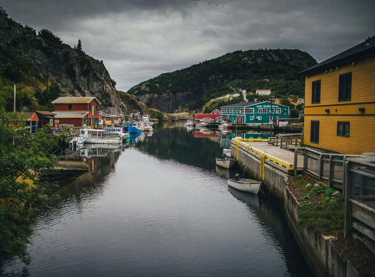 A narrow Newfoundland harbour lined with fishing stages, small boats and painted wooden buildings under a dark sky.