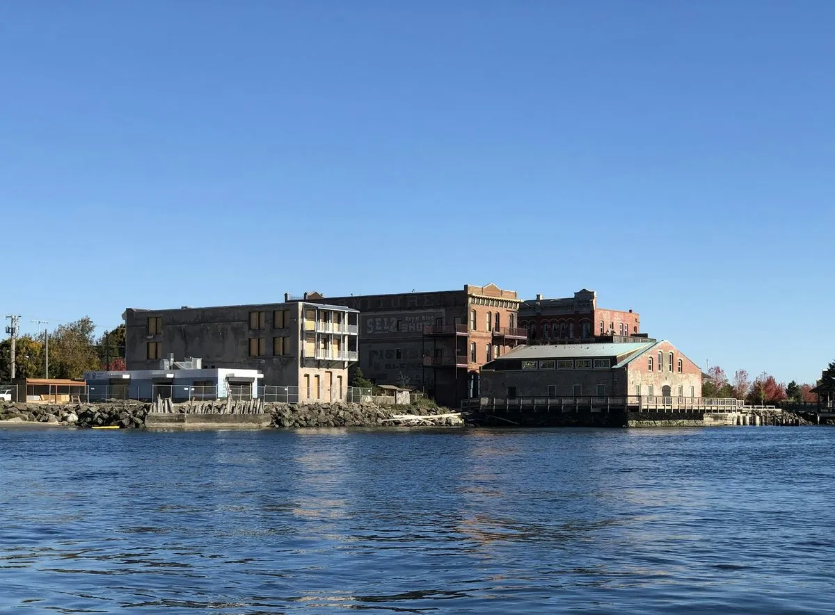 Brick Victorian buildings line the Port Townsend waterfront, seen from the water under a clear blue sky.