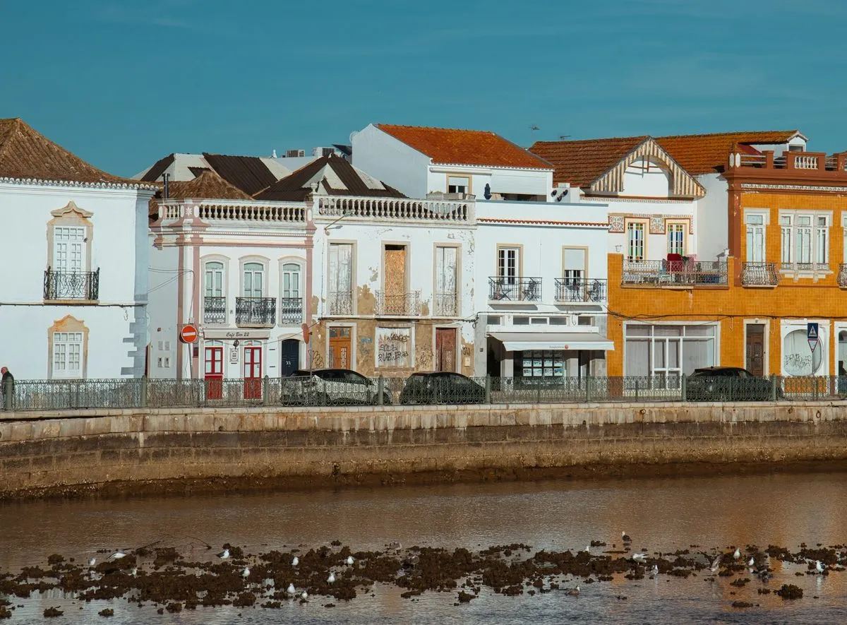 White, tiled and ochre townhouses along the river in Tavira at low tide.