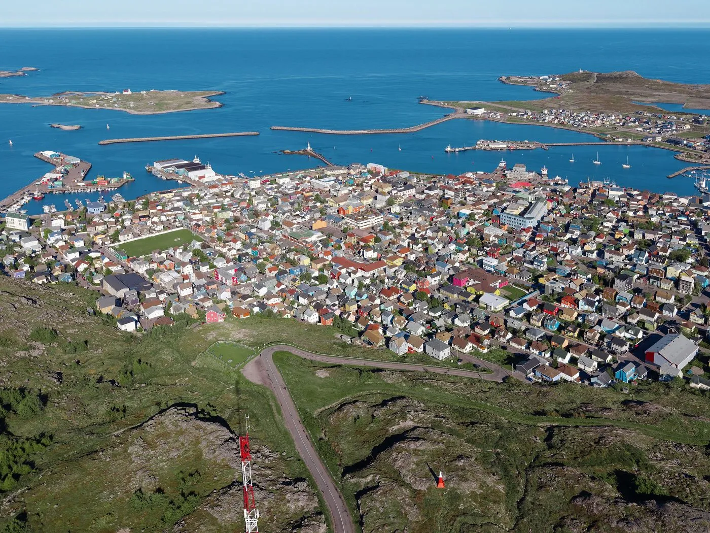 The town of Saint-Pierre from the air, a tight cluster of brightly painted houses beside a harbour, with small islands beyond.