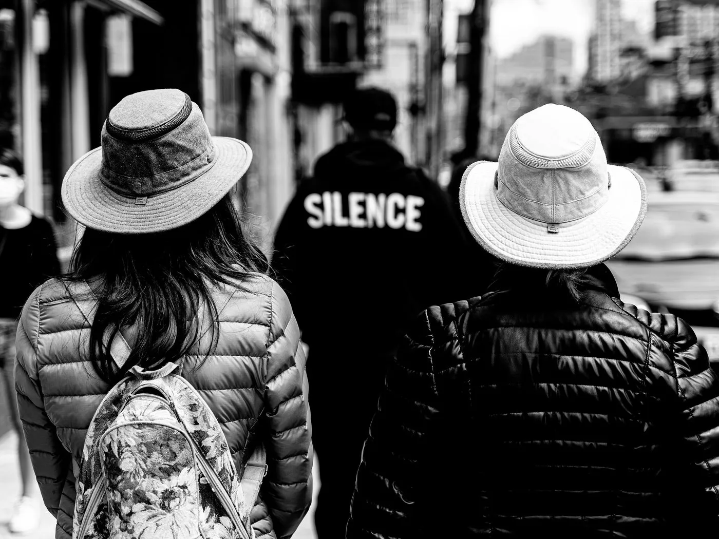 Black and white photo of two people seen from behind on a city street, each wearing a wide-brimmed Tilley hat.
