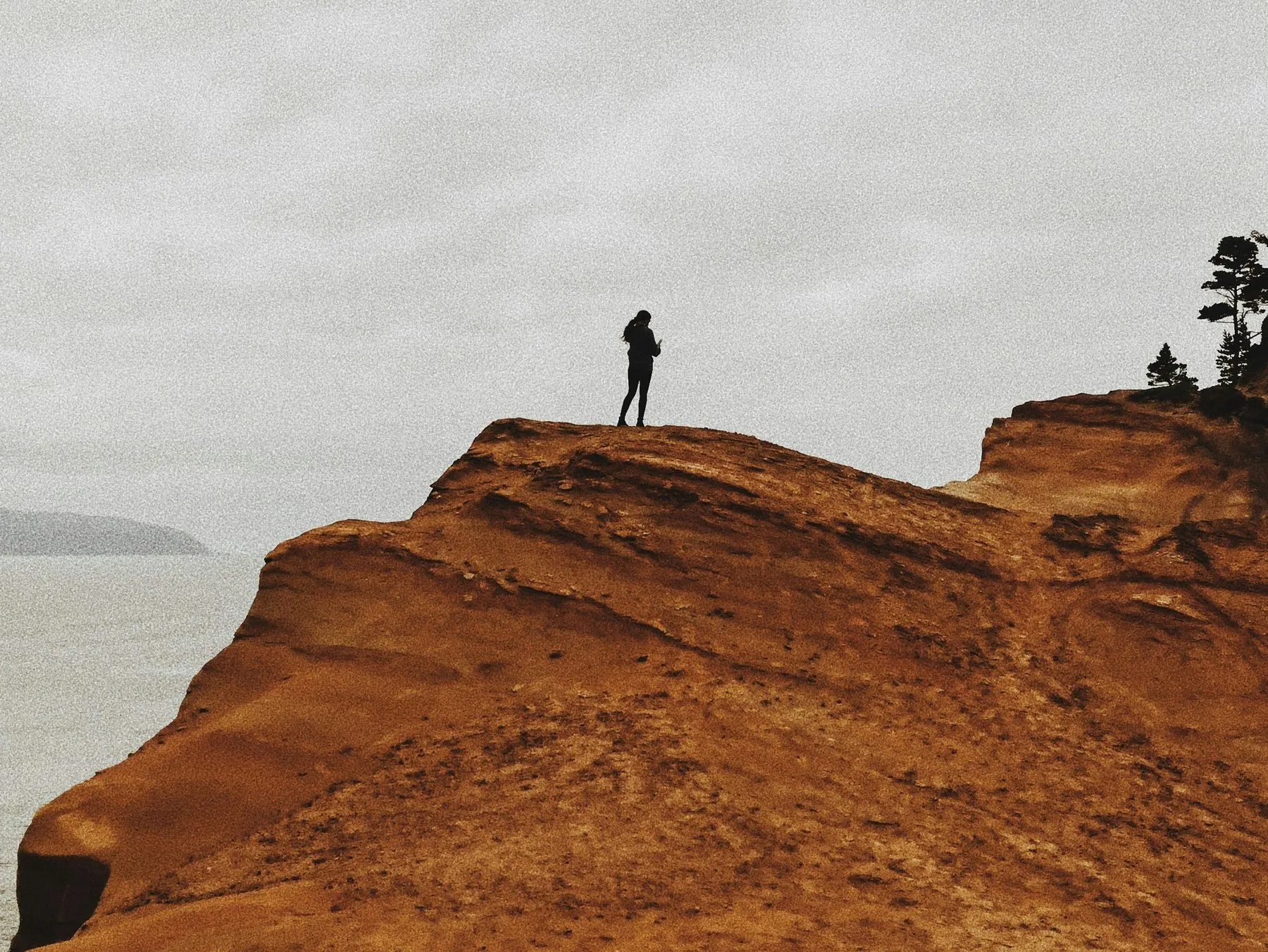 A lone figure standing at the edge of an orange sandstone cliff in the fog.