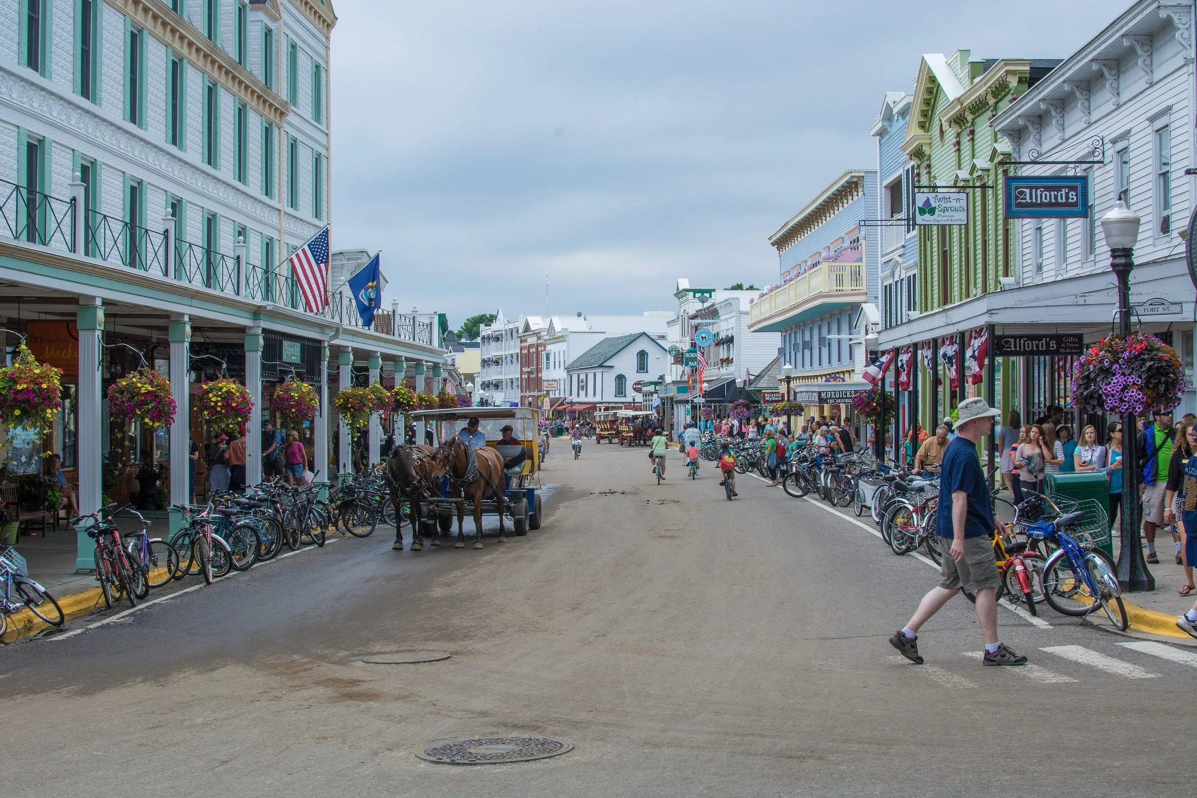 Main Street on Mackinac Island, lined with hundreds of parked bicycles, with a horse-drawn carriage in the road, people walking and no cars.