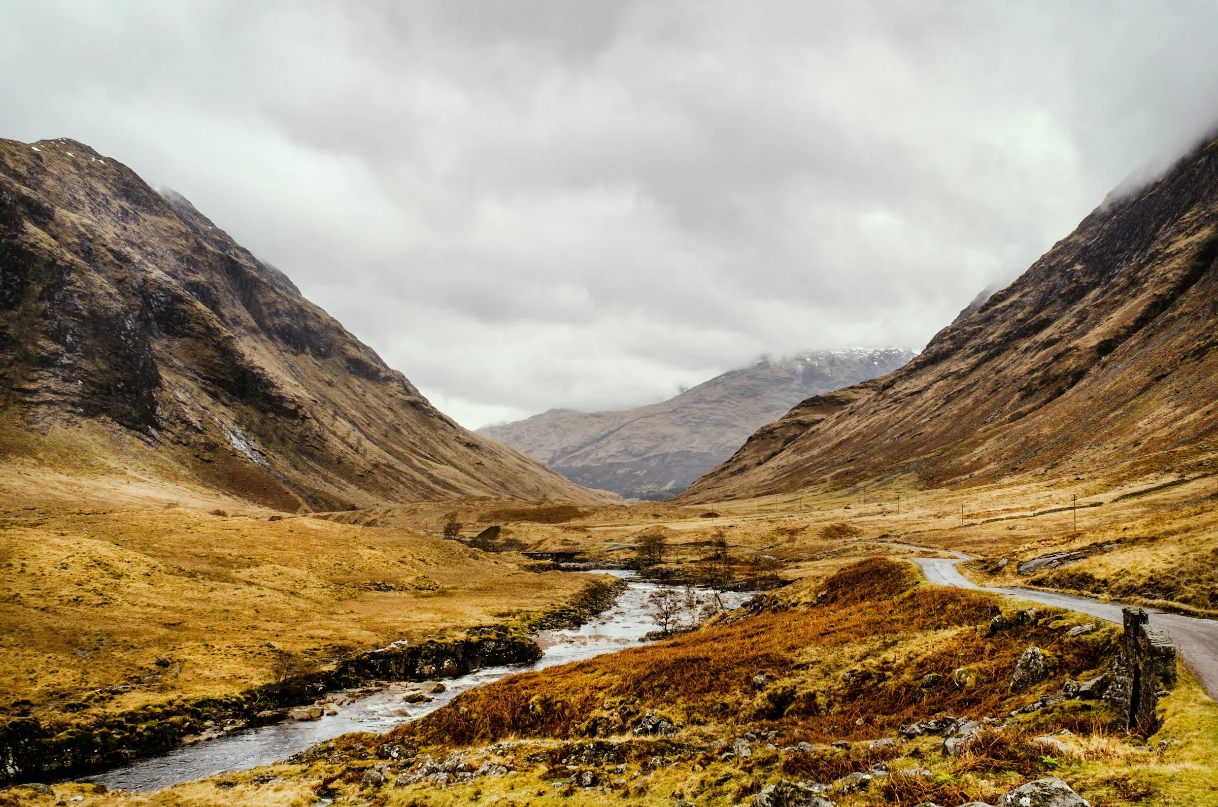 Glen Etive in autumn colours, with the river on the left and a single-track road winding down the glen under low cloud.