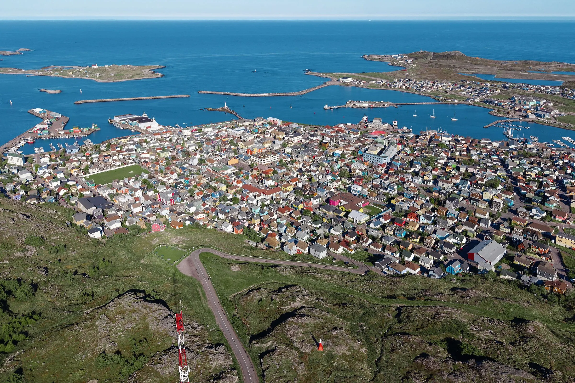 The town of Saint-Pierre from the air, a tight cluster of brightly painted houses beside a harbour, with small islands and open sea beyond.