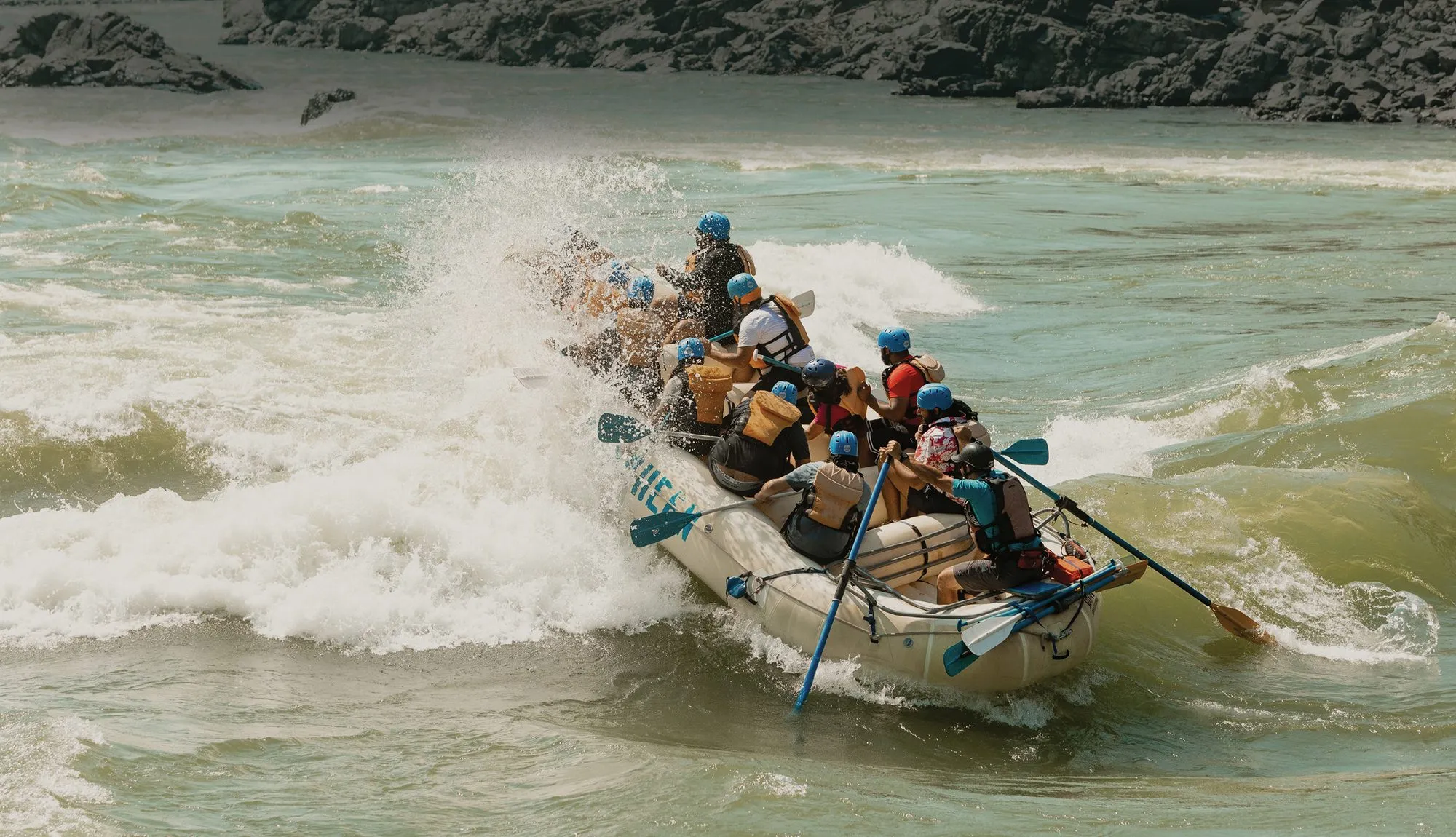 A raft full of people in blue helmets drops into a large breaking wave on the Thompson River.
