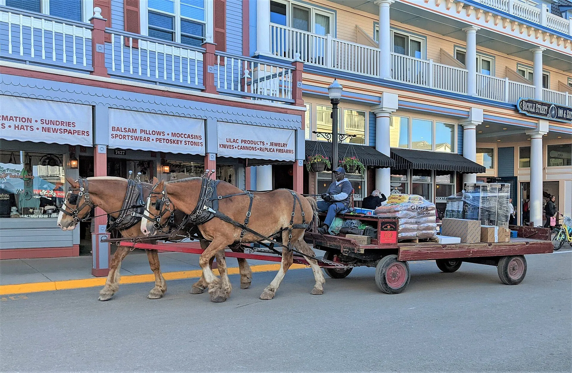 Two draft horses pulling a flatbed wagon loaded with boxes and sacks along Main Street.