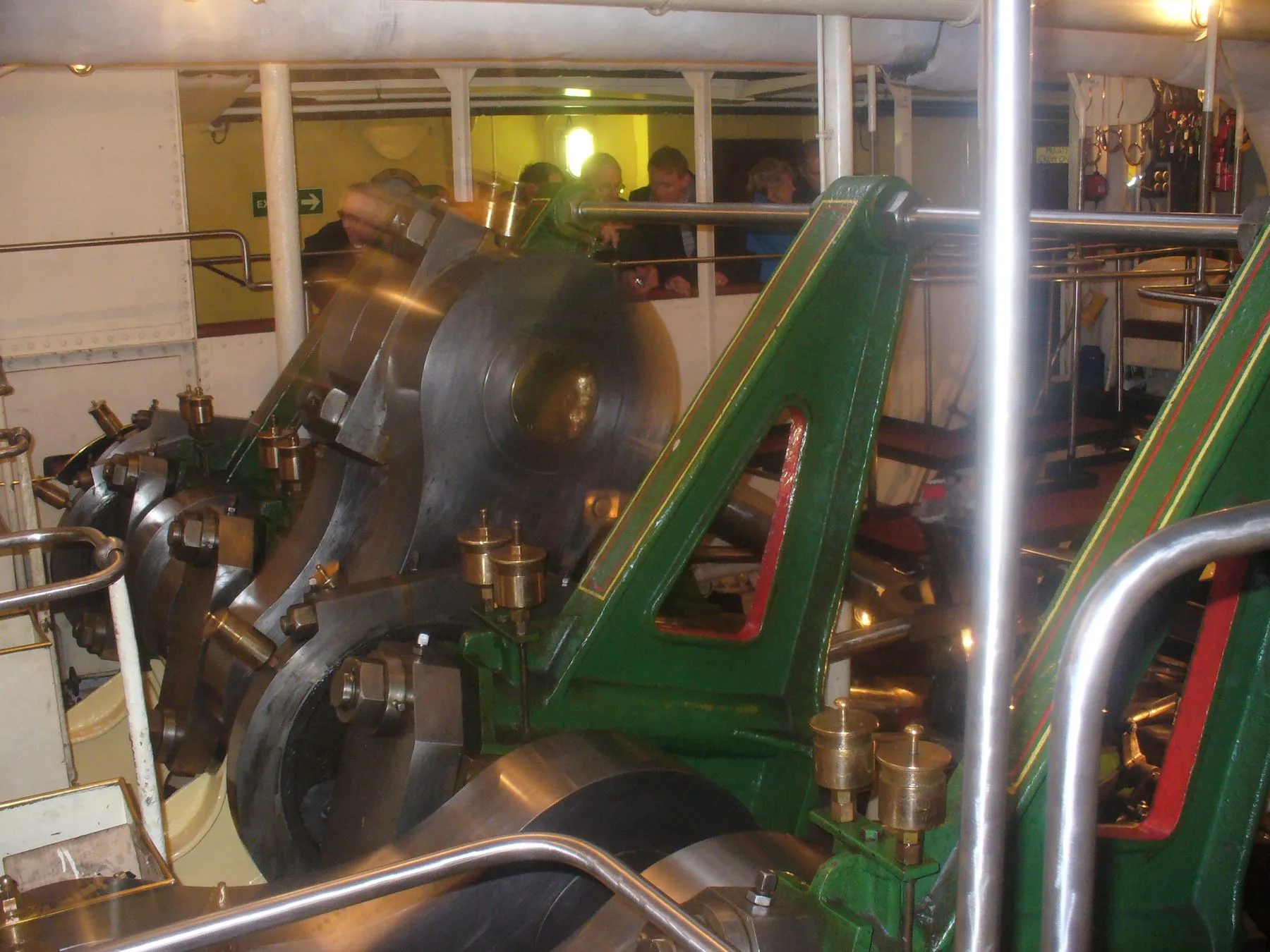 The polished steel cranks and green-painted frames of Waverley’s steam engine, with passengers watching from behind a rail.