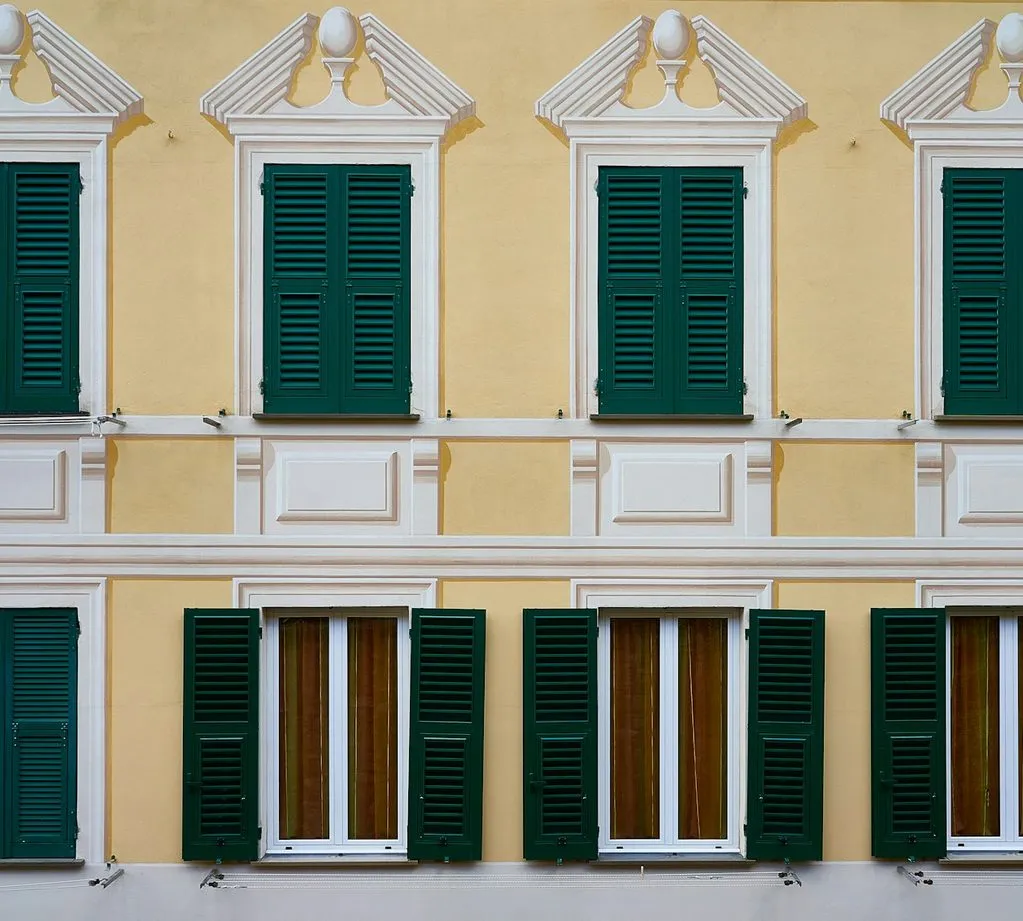 A yellow house front in Camogli with green shutters and ornate white window surrounds.