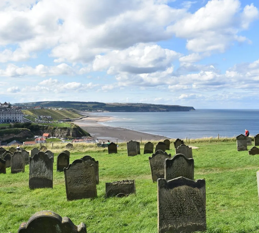 Weathered headstones in the clifftop churchyard at Whitby, looking across the bay.
