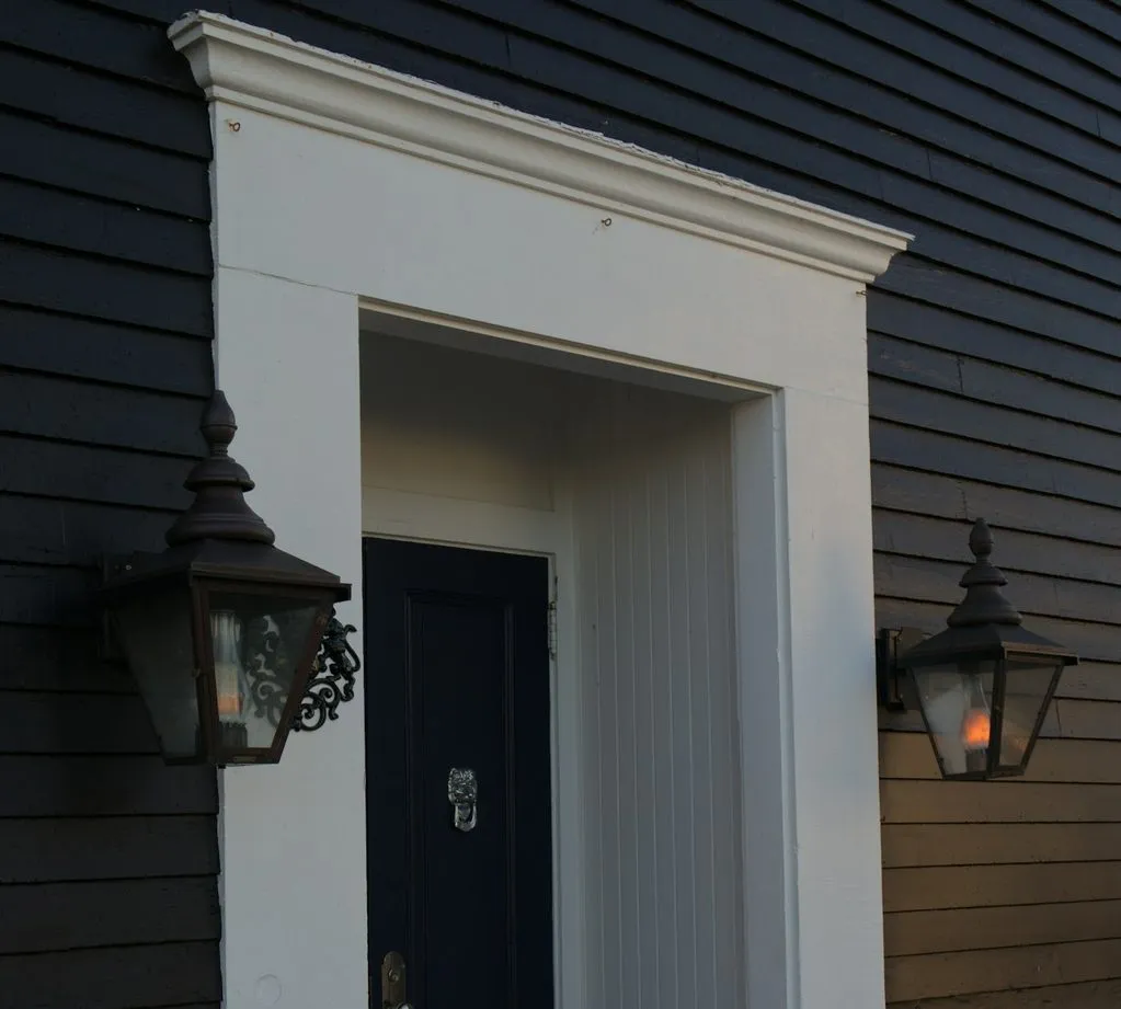 A sheltered front doorway with white trim and two lanterns on a dark-sided house.