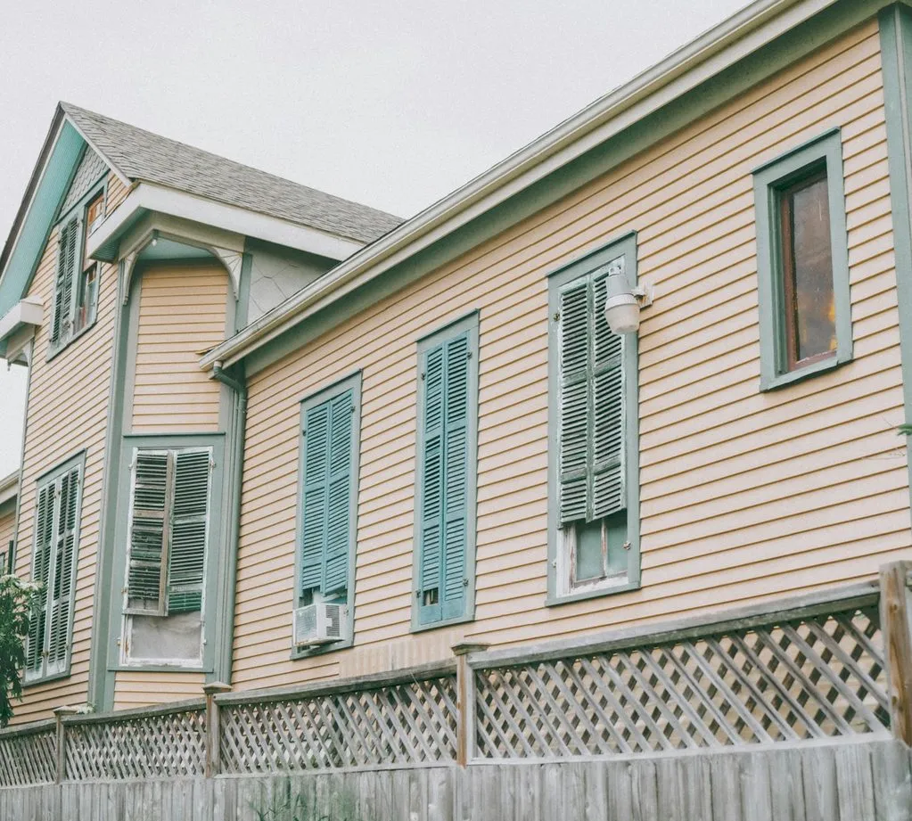 A peach-coloured wooden house with green shutters in Galveston, raised on a lattice-skirted foundation behind a weathered fence.
