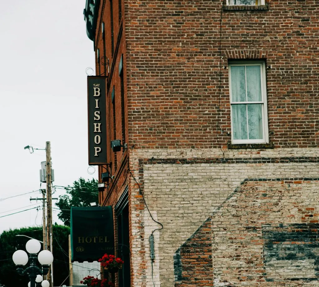 The corner of a red-brick Victorian hotel in Port Townsend, with a hanging sign reading Bishop and faded paint on the wall.
