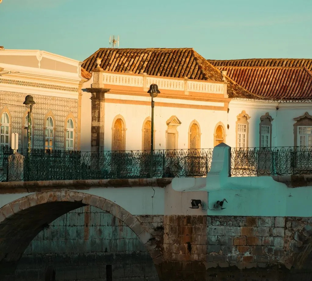 An arch of Tavira’s old bridge, with tile-roofed townhouses behind it in warm evening light.