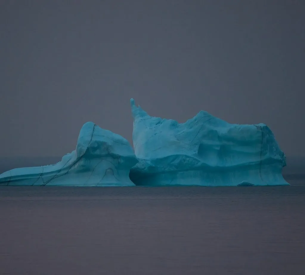 A blue iceberg drifting off Twillingate, Newfoundland, under a grey sky.