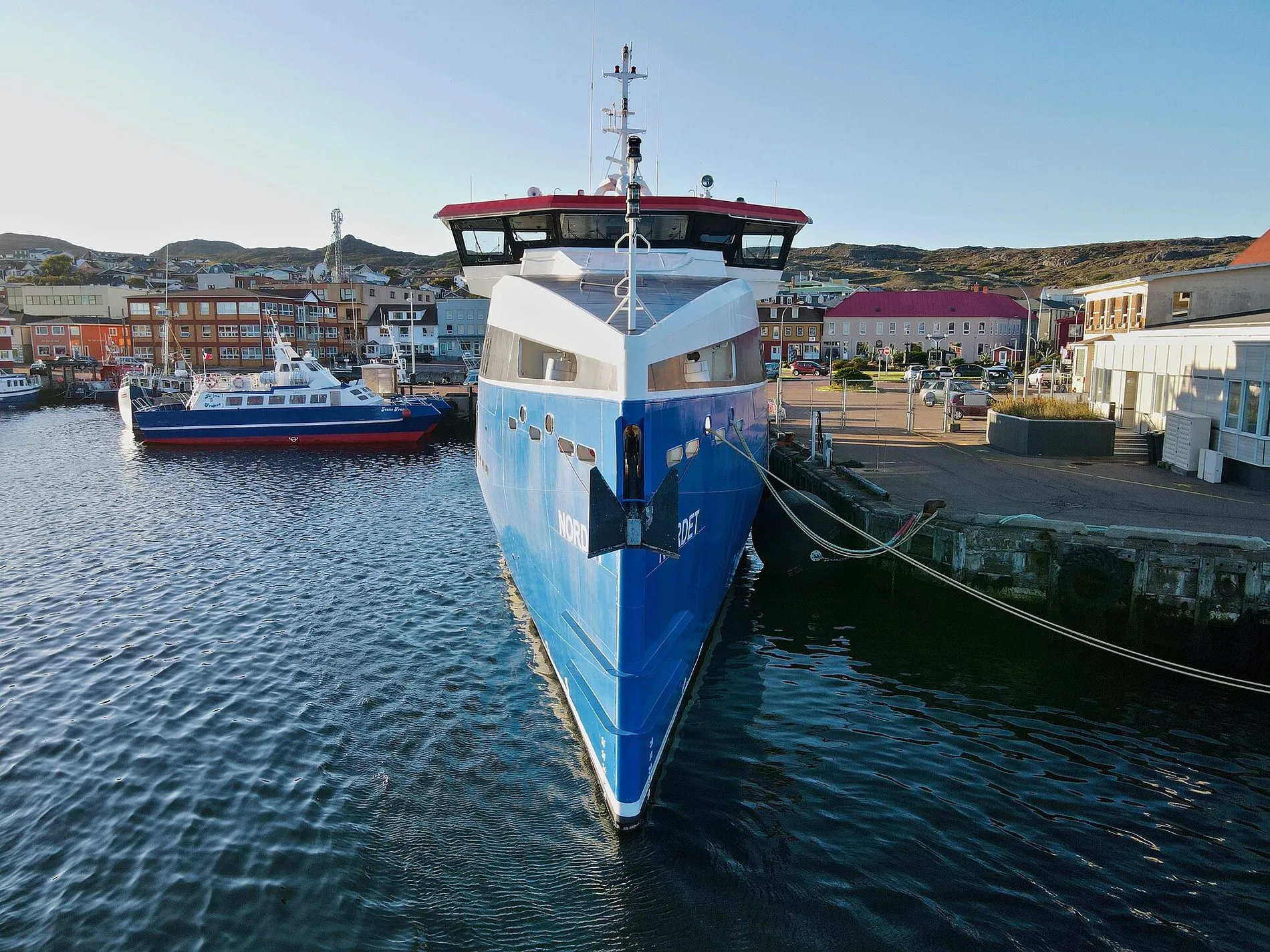 A blue and white ferry moored at the quay in Saint-Pierre, with the town’s painted buildings behind it.