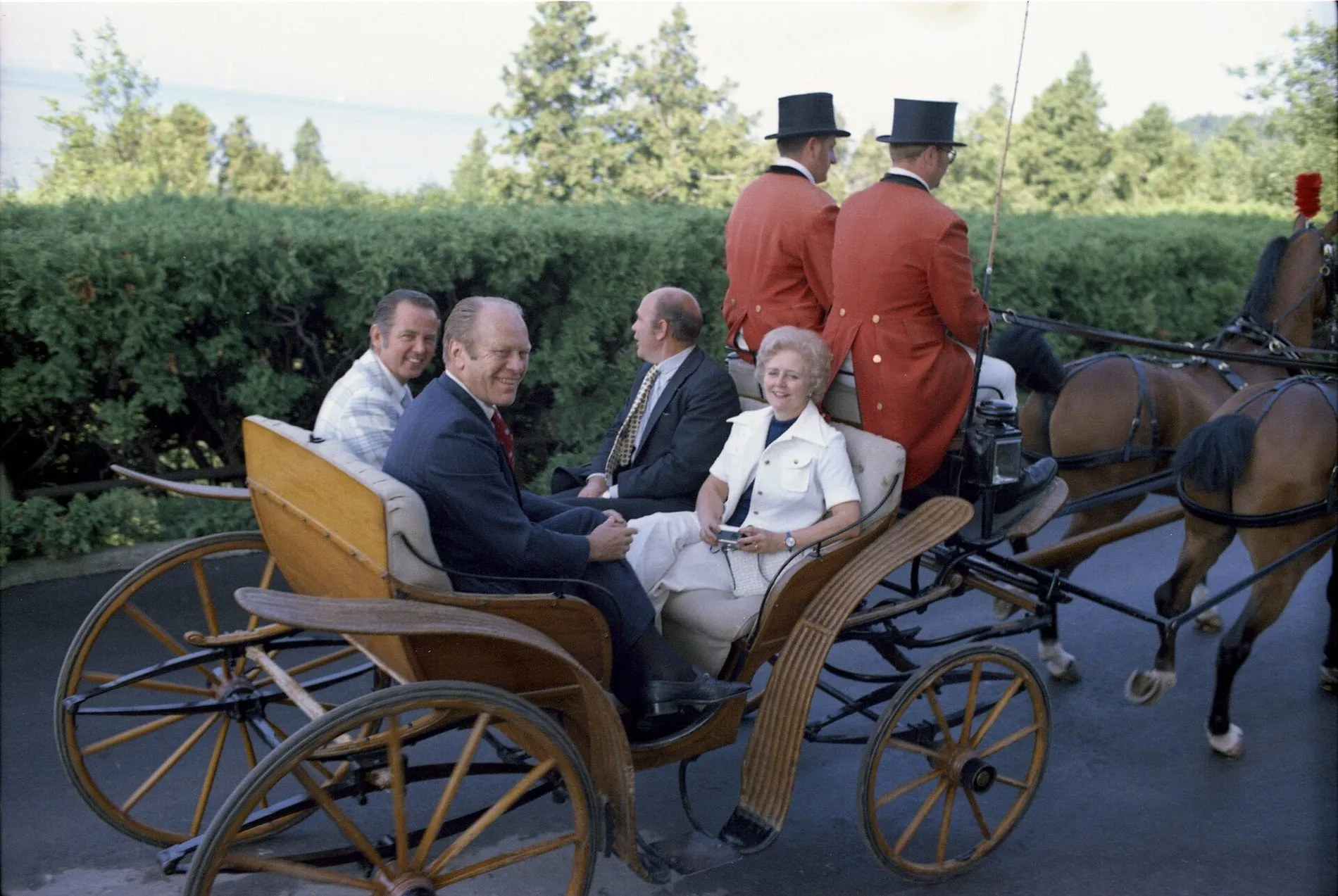 President Gerald Ford and his party seated in an open horse-drawn carriage, with two coachmen in red coats and top hats.
