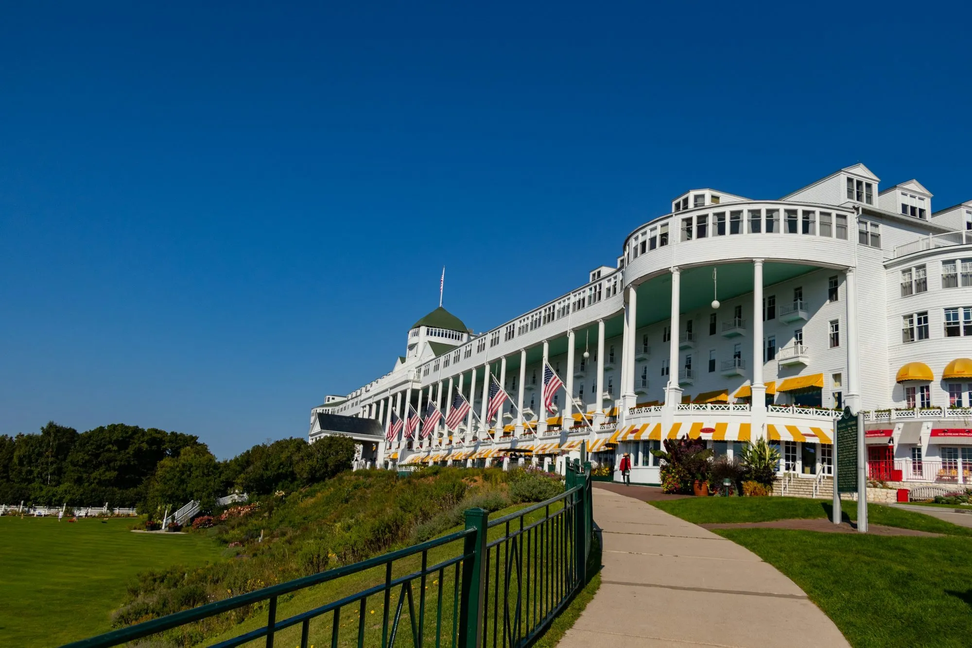 The long white colonnaded porch of the Grand Hotel on Mackinac Island, hung with flags and yellow awnings, under a deep blue sky.