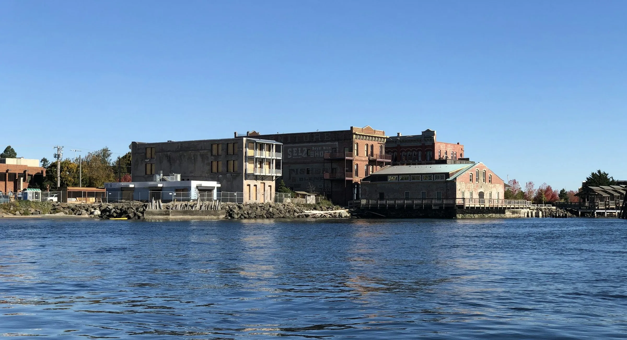 Brick Victorian buildings line the Port Townsend waterfront, seen from the water under a clear blue sky.