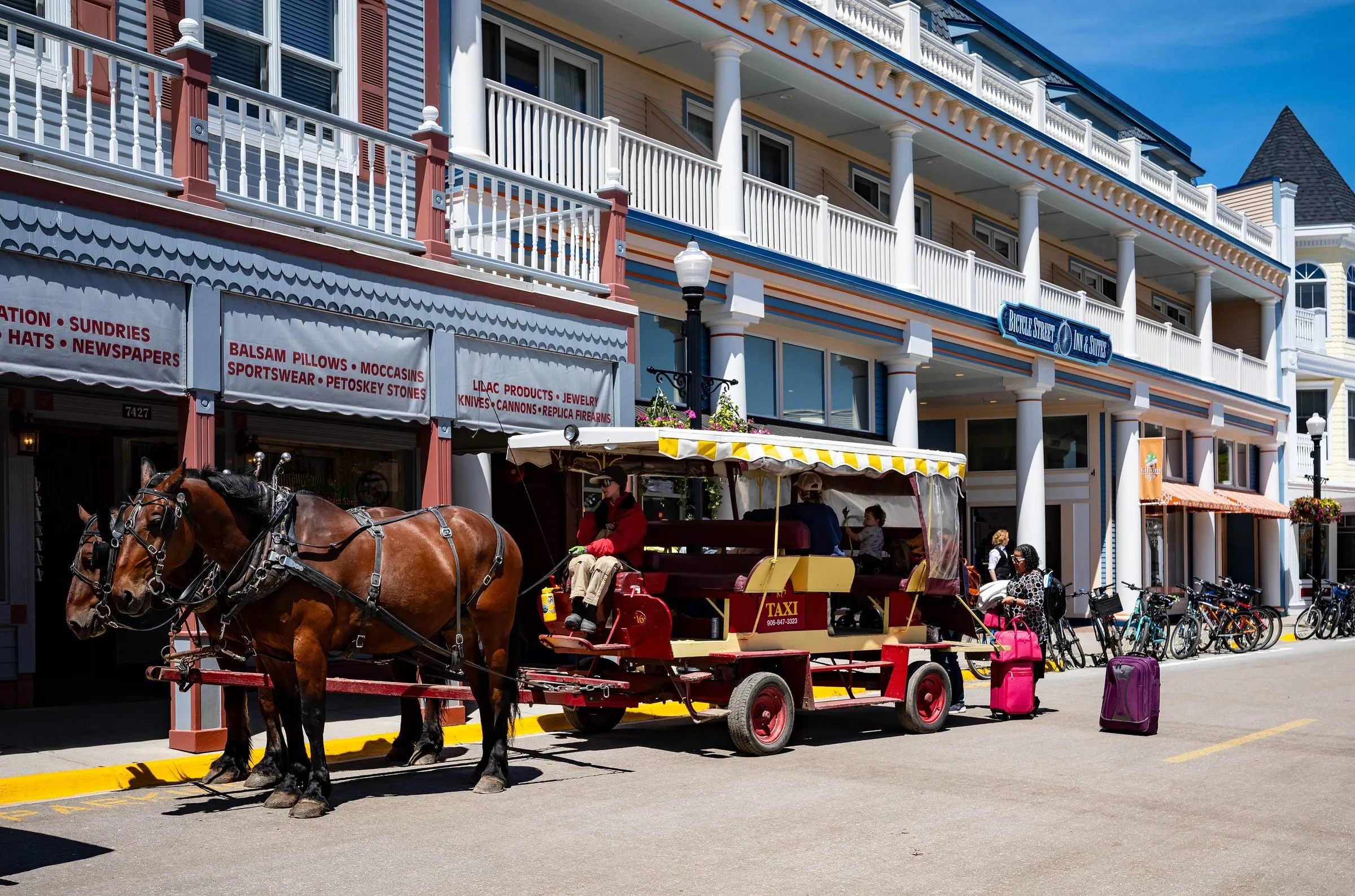 A horse-drawn taxi with a yellow canopy waiting outside a hotel on Main Street, with suitcases on the pavement beside it.
