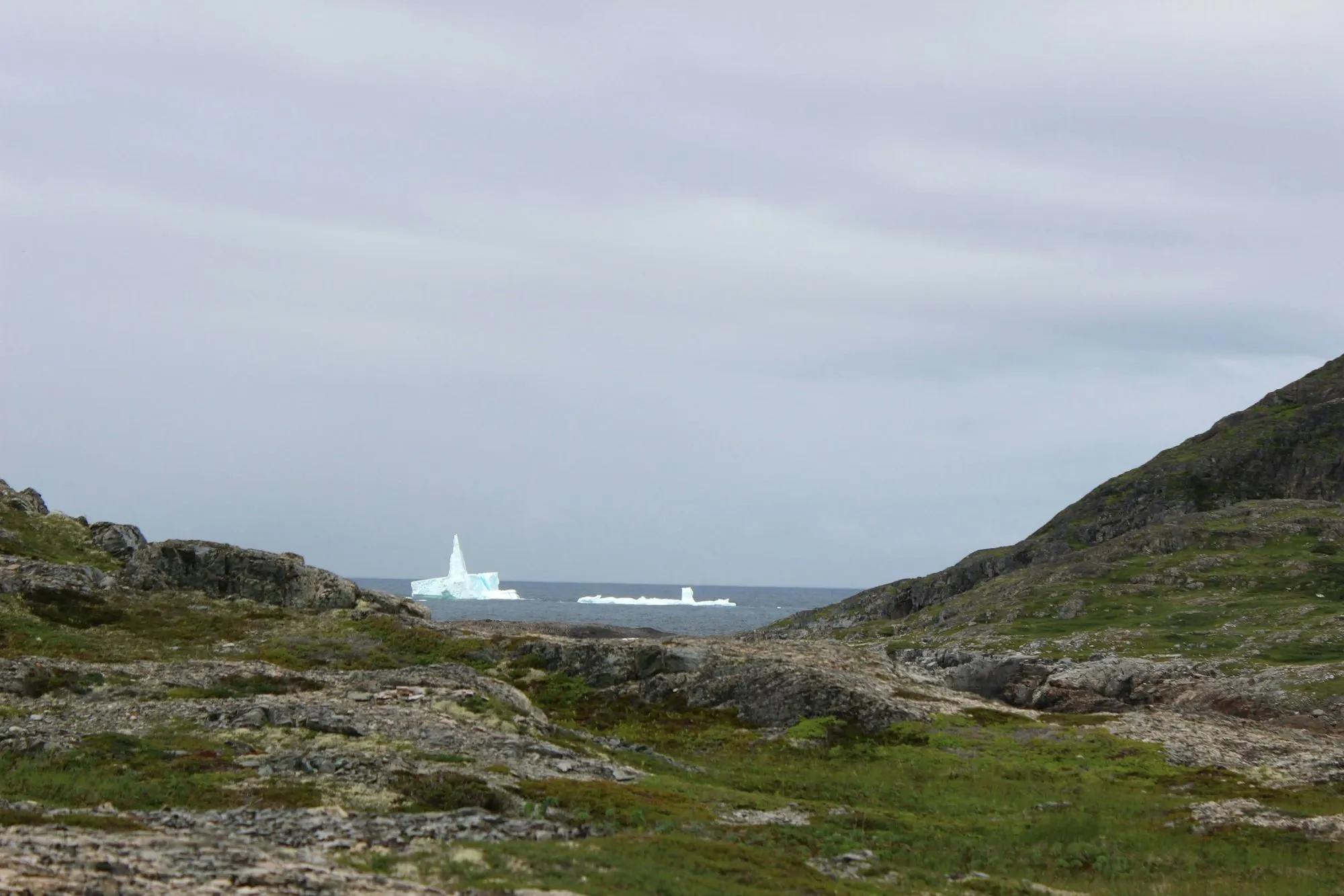 An iceberg at sea, seen through a gap between two rocky green slopes at Brimstone Head.