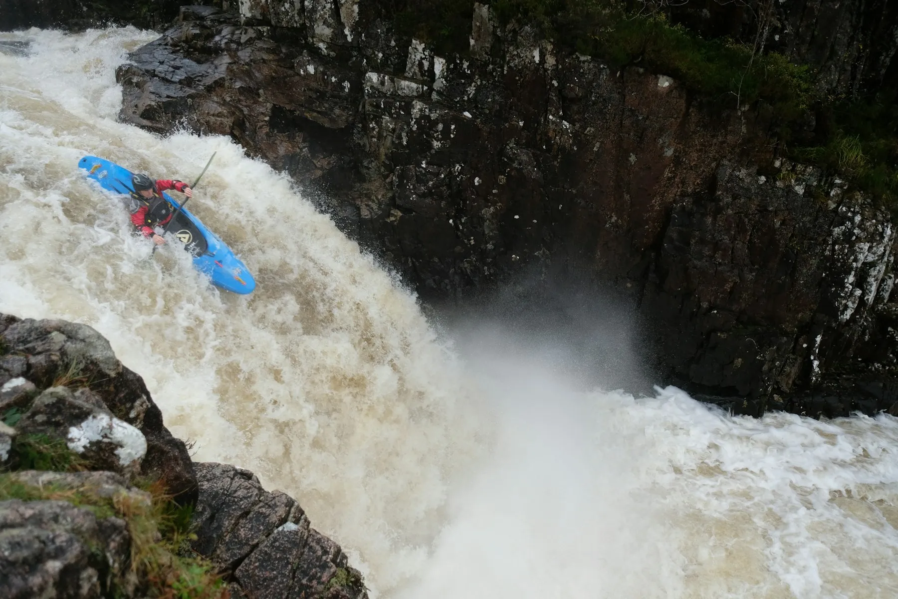 A kayaker in a blue boat going over a large waterfall on the River Etive.