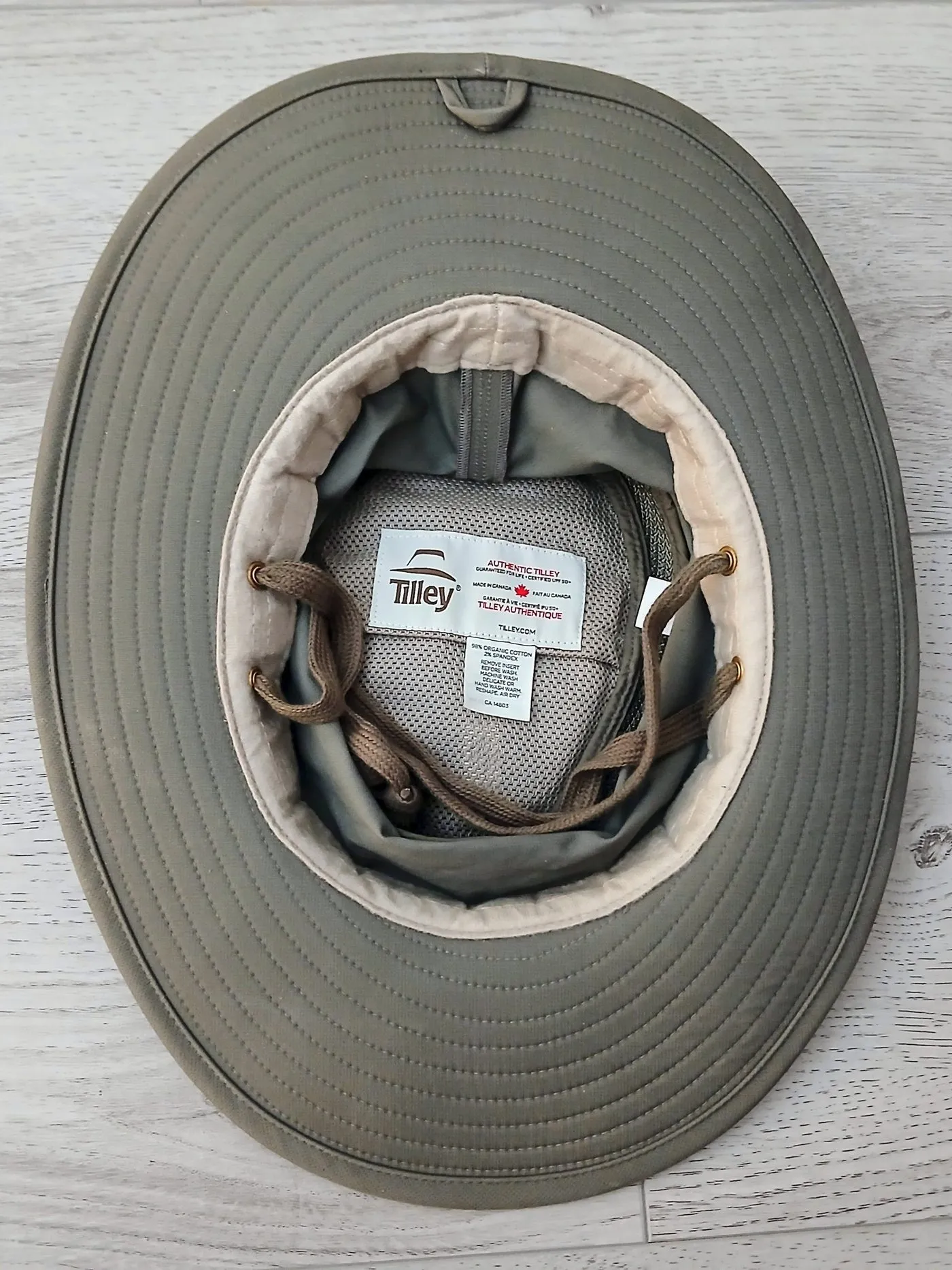 Looking up into an olive Tilley hat, showing the white Tilley label, the mesh lining and the brown cords tucked into the crown.
