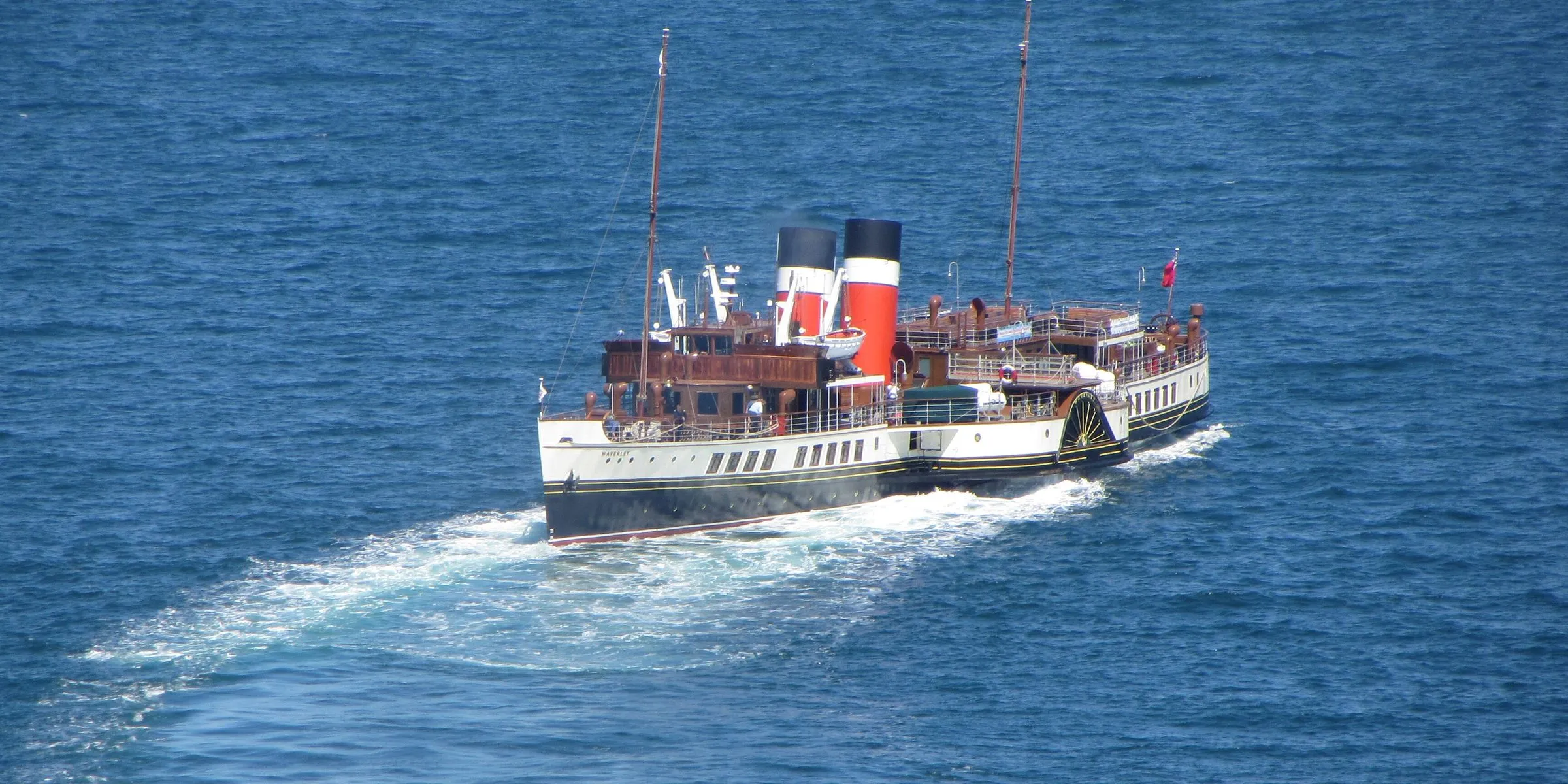 Waverley seen from above on bright blue sea, leaving a long curved white wake as she turns.