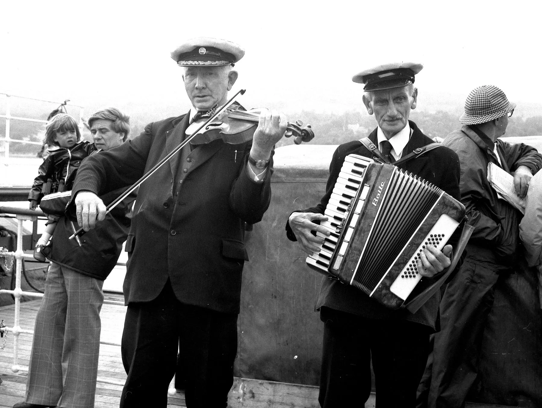 A black and white photo from 1978 of two men in peaked caps playing a fiddle and an accordion on Waverley’s deck.