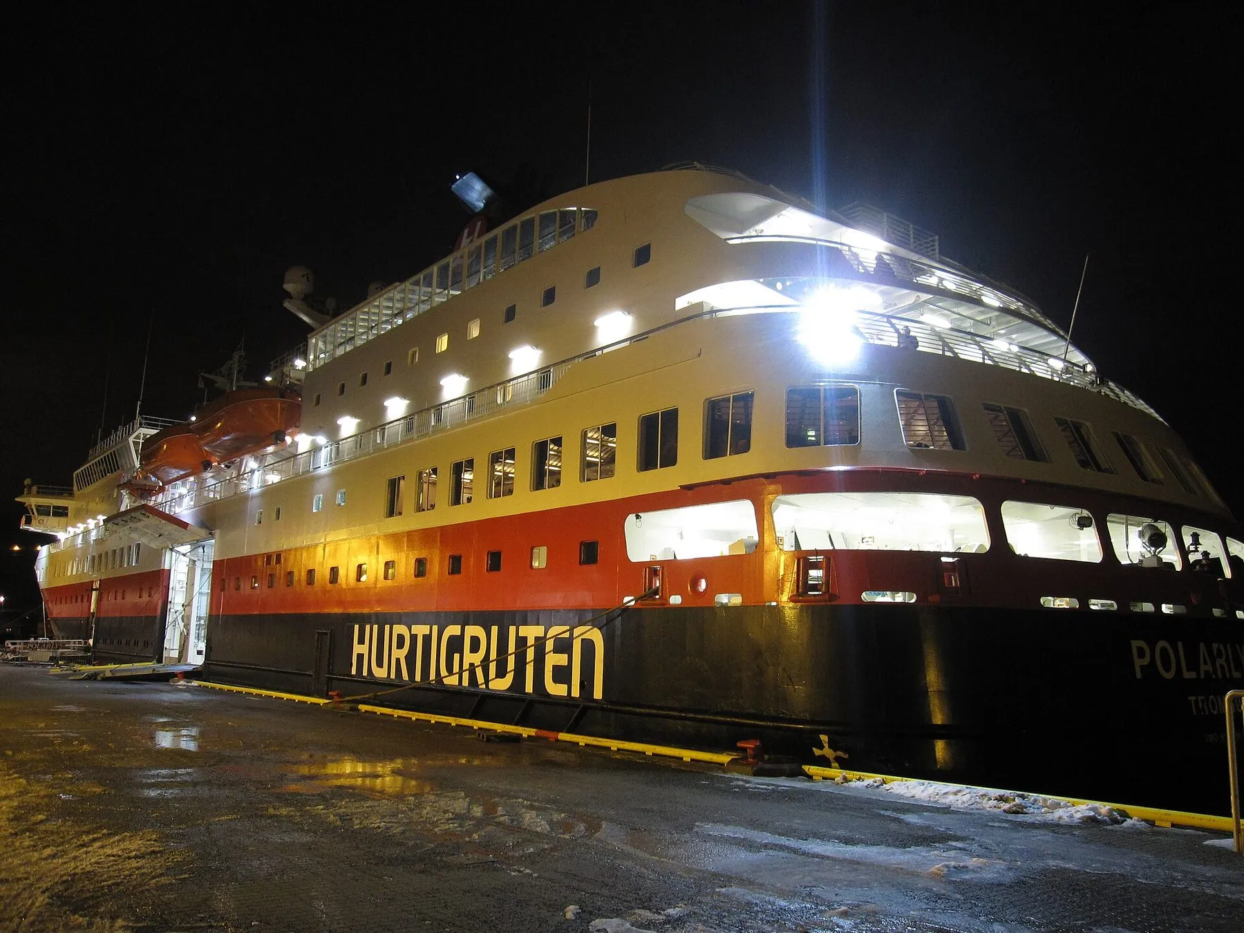 The Hurtigruten ship MS Polarlys lit up at a wet quay at night.