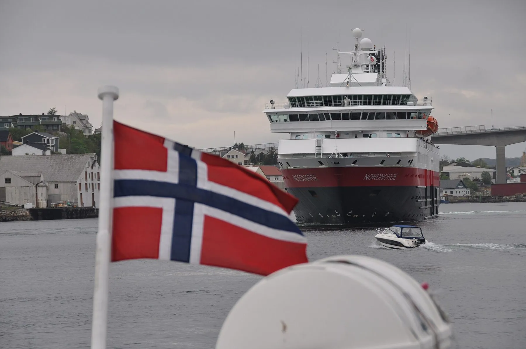 MS Nordnorge seen from another boat, with a Norwegian flag flying in the foreground.