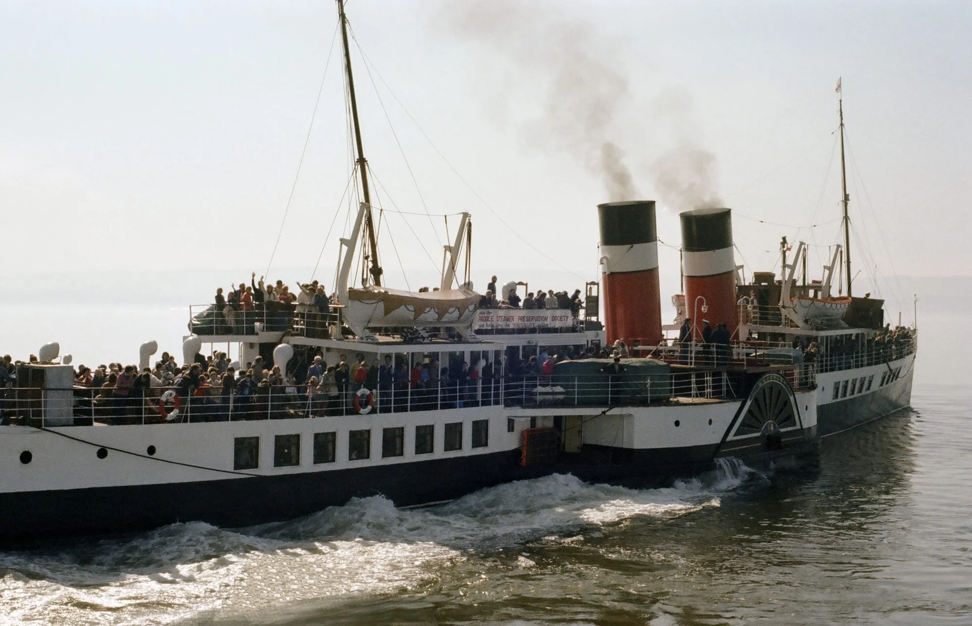 Waverley leaving a pier with decks crowded with passengers, smoke coming from her funnels and water churning at the paddle box.