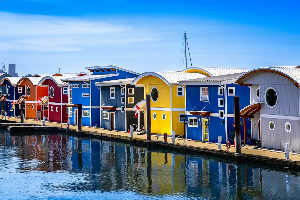 A row of brightly painted float homes along a dock, reflected in still water.