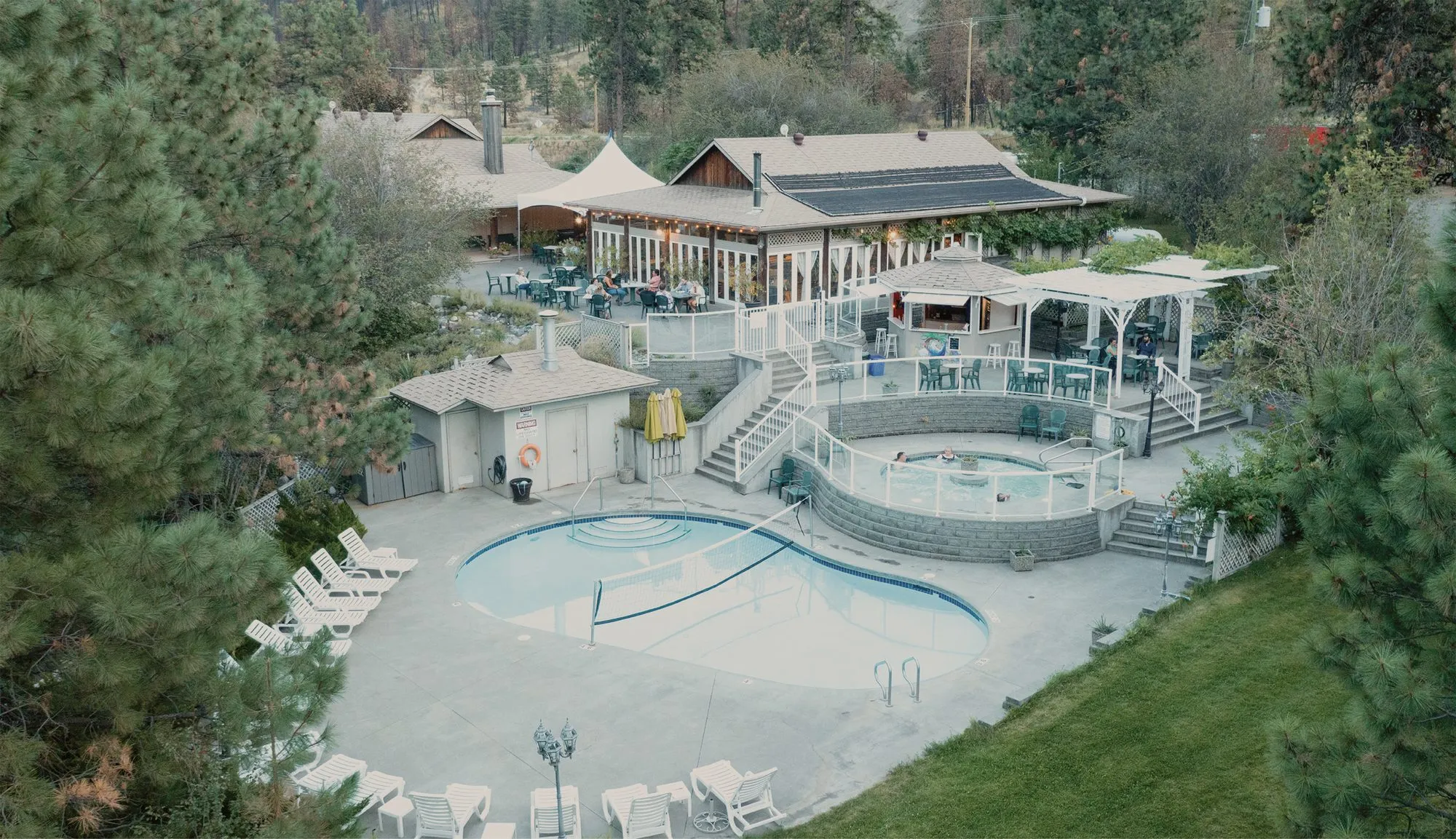 Looking down on the resort’s curved pool, a raised hot tub and a restaurant deck among pine trees.