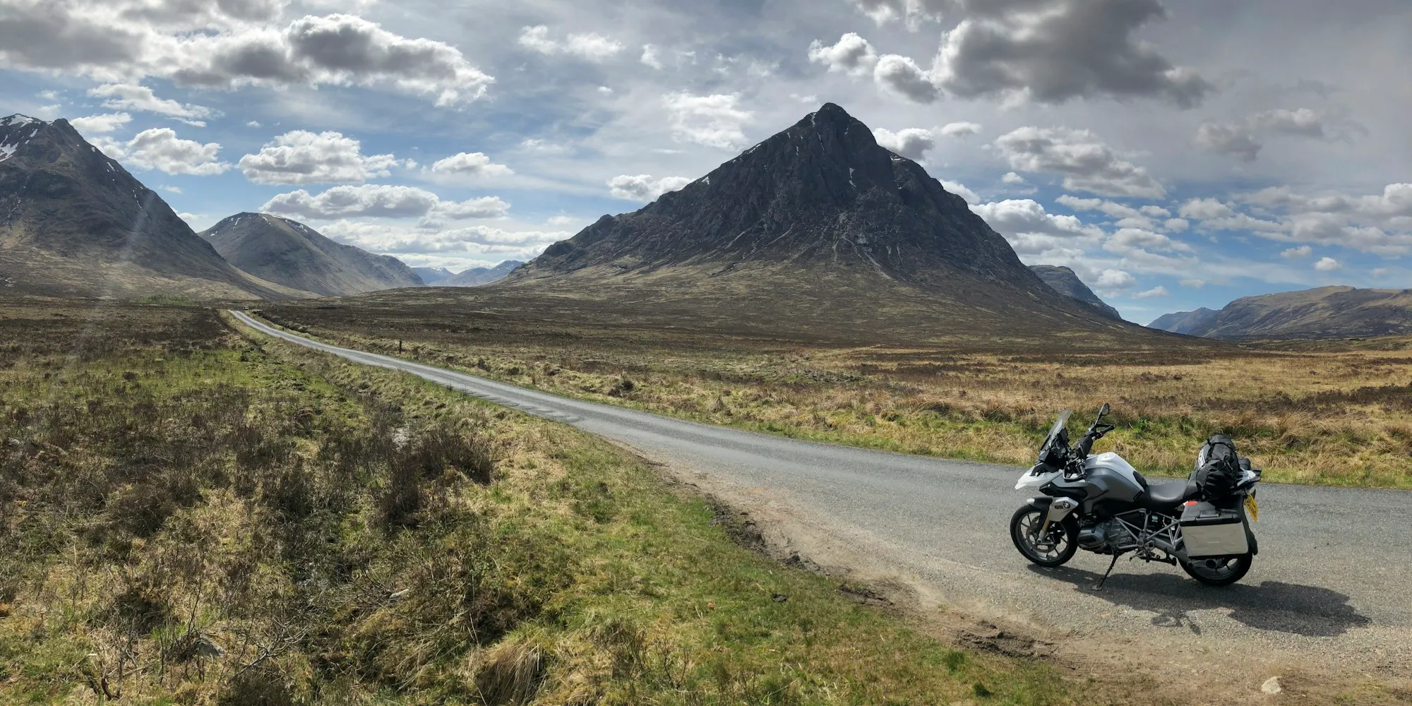 A motorcycle parked beside a single-track road across moorland, with the pyramid of Buachaille Etive Mòr behind.