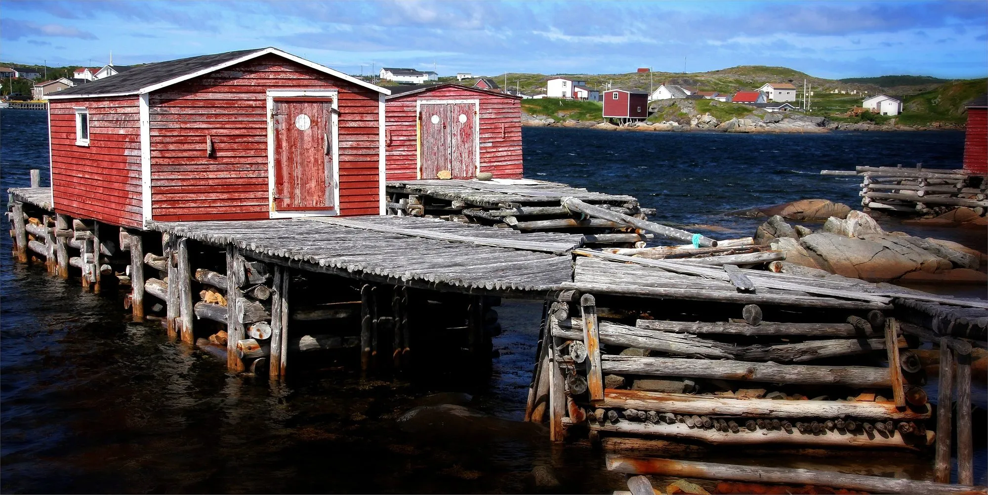 Red wooden fishing sheds on a weathered timber wharf built out over the water.