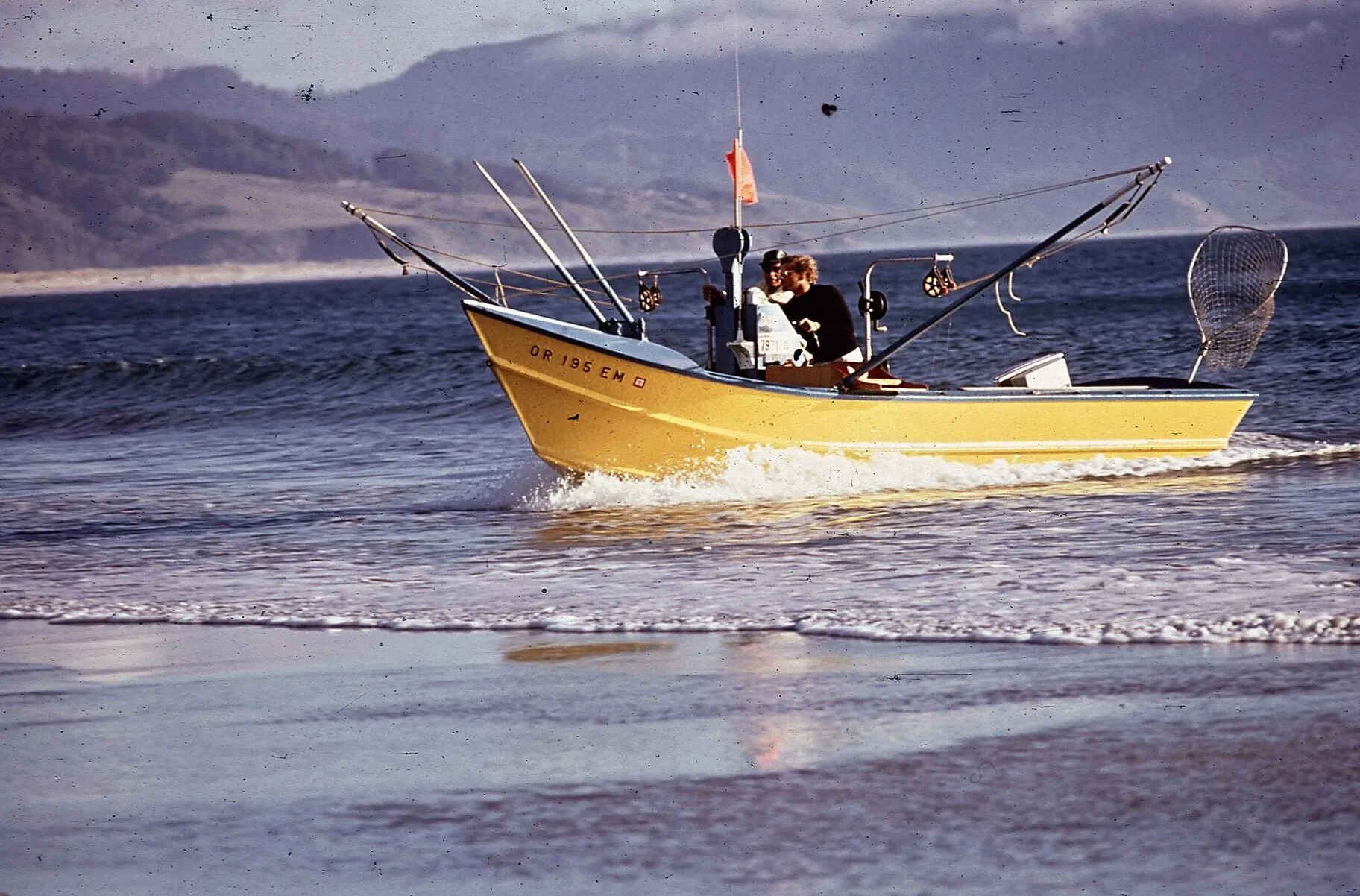 A yellow dory with its crew aboard riding in through the surf towards the beach.