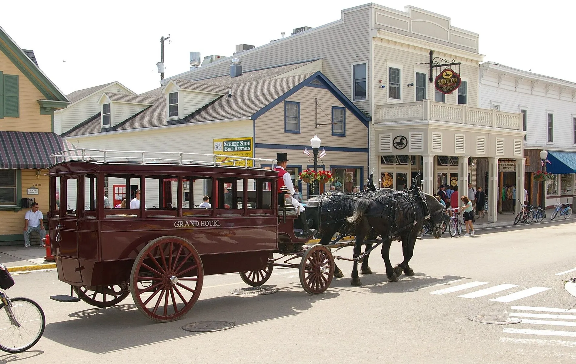 A dark red horse-drawn omnibus lettered Grand Hotel, pulled by two black horses along Main Street.
