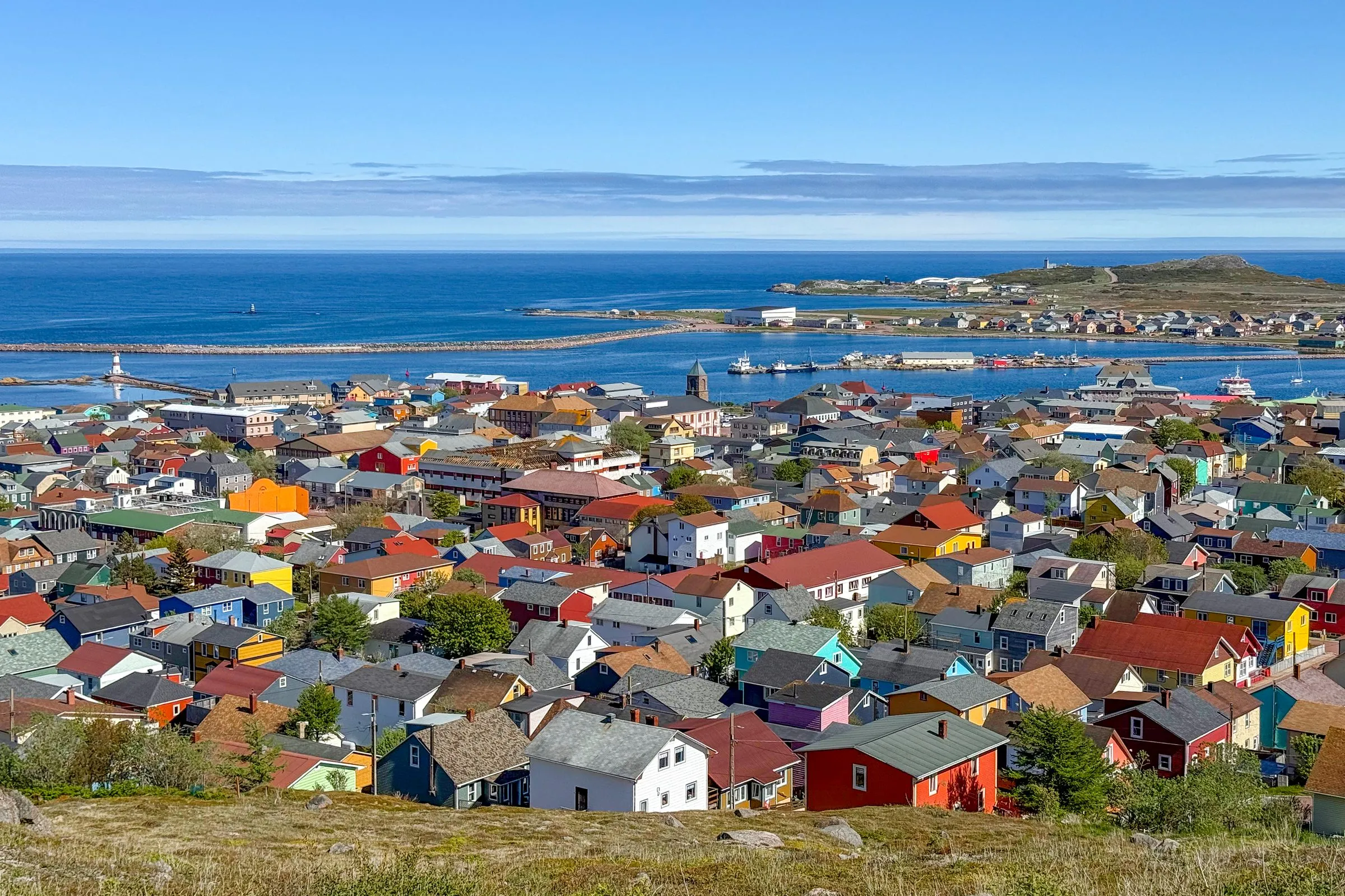 Hundreds of brightly painted rooftops running down to the harbour at Saint-Pierre, with a low island and the sea beyond.