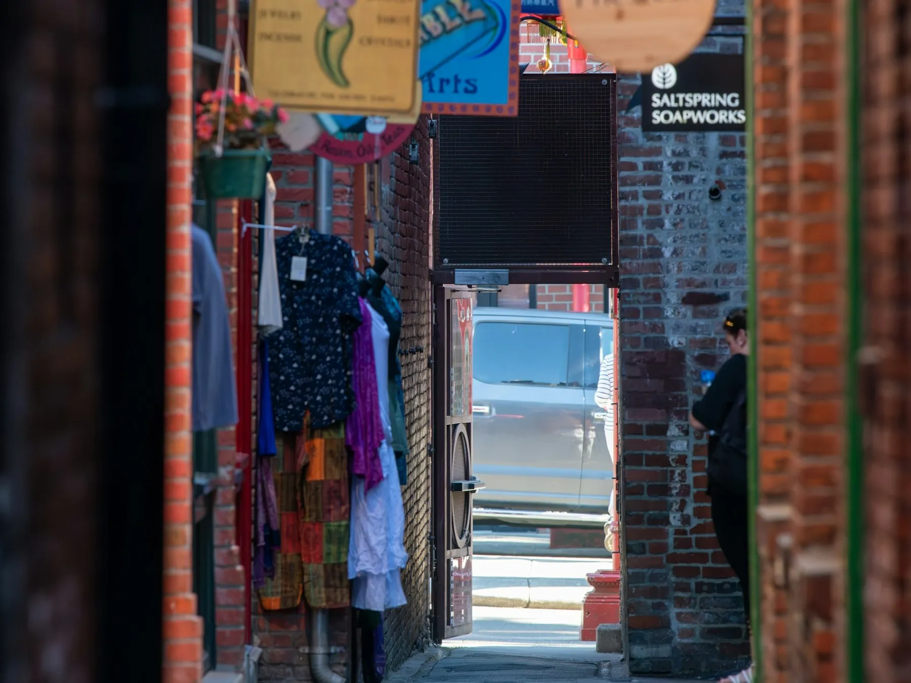 Shop signs and colourful clothing displays line a narrow brick pedestrian alley in Victoria, British Columbia.