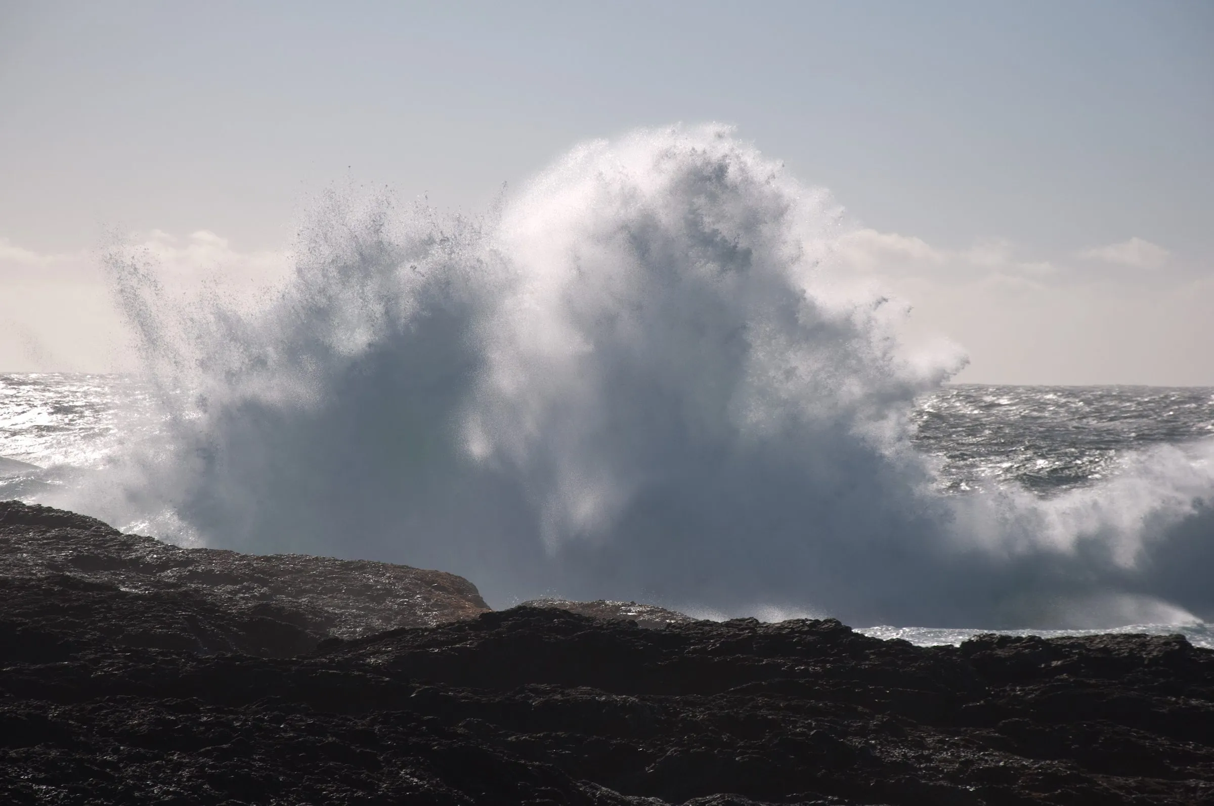 A huge wave exploding into white spray against dark rocks off Chesterman Beach.